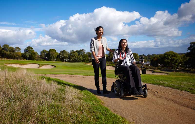 One woman walking one in power wheelchair on golf course