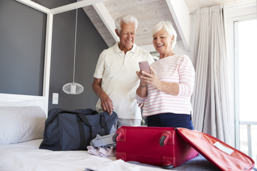 Couple with suitcase on bed containing holiday incontinence supplies.