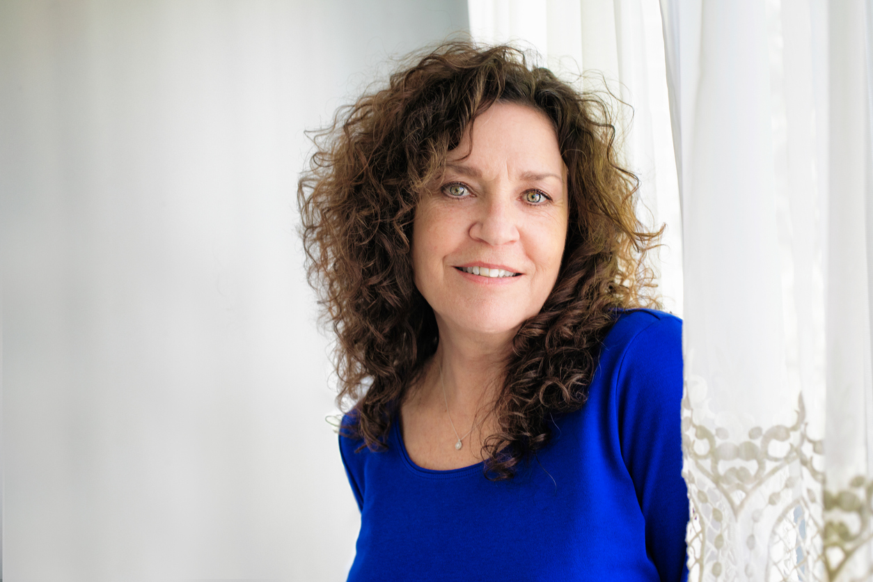 Cheerful mature Caucasian female portrait by window skin at risk