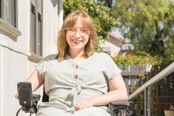 Woman outdoors, smiling, using a powered wheelchair.